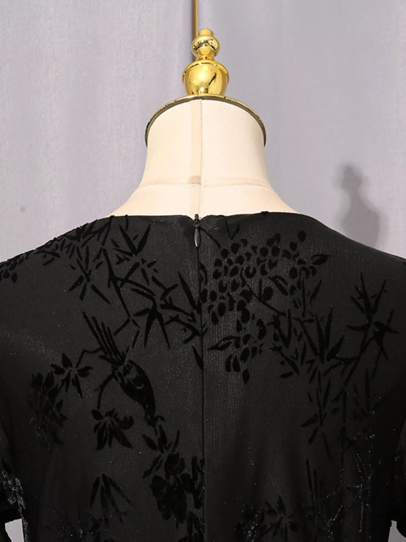 Black embroidered lace dress displayed on a cream dress form with a gold finial, showing the back view with floral and bird motifs.