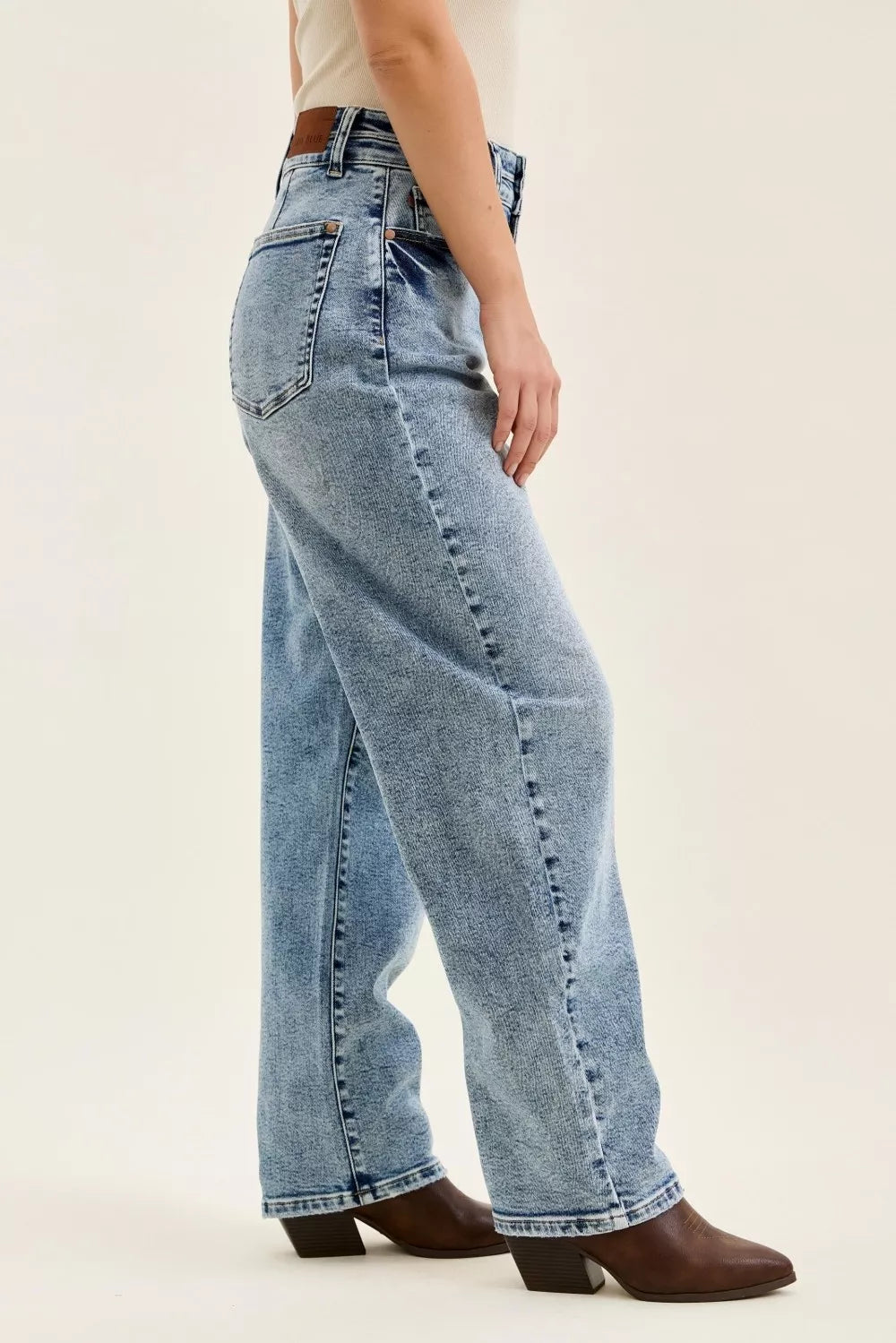 Person wearing light blue jeans and brown boots on a plain background