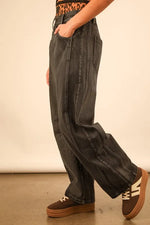 Person wearing wide-leg jeans and brown shoes on a plain background