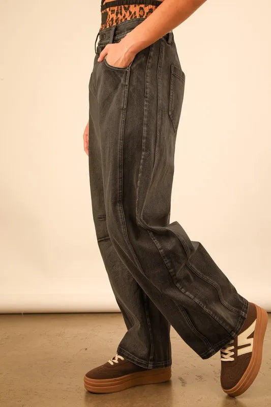 Person wearing wide-leg jeans and brown shoes on a plain background