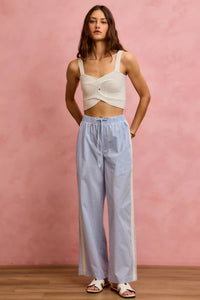 Woman wearing a white top and light blue checkered pants against a pink background
