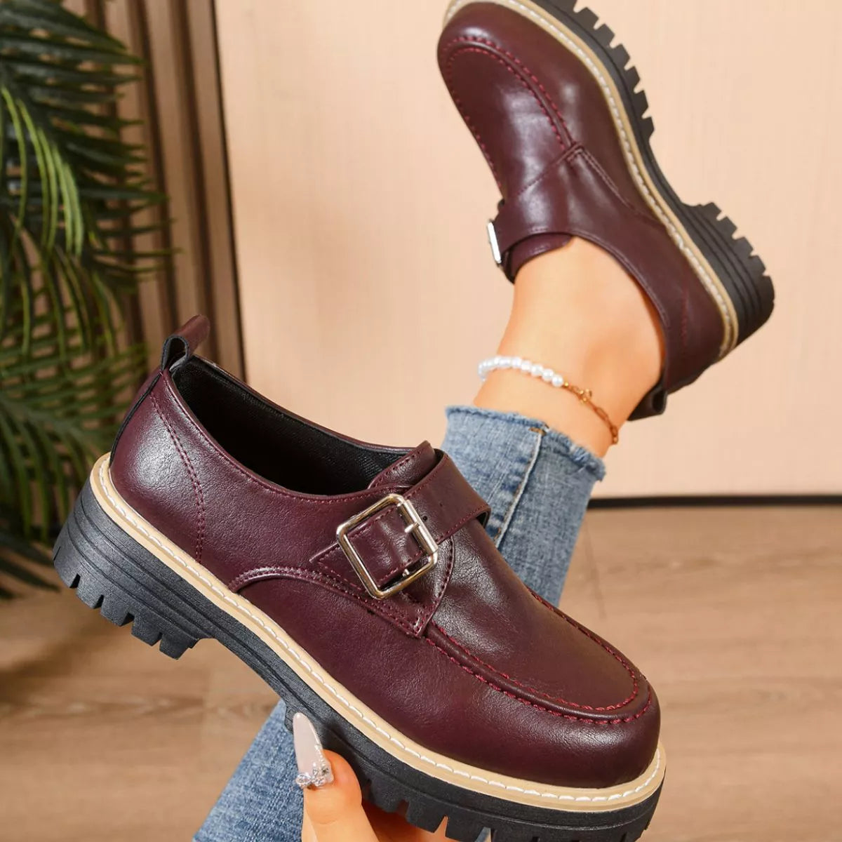 Brown leather shoes with a buckle worn by a person on a neutral background