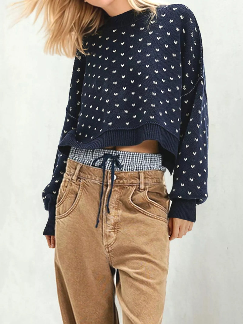 Person wearing a navy blue patterned sweater with a checkered shirt and beige pants on a white background