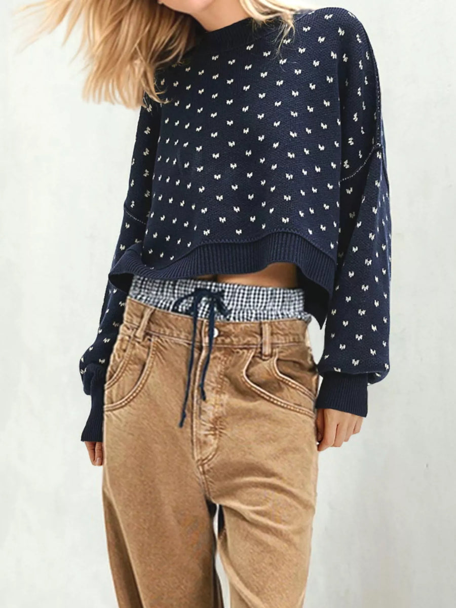 Person wearing a navy blue patterned sweater with a checkered shirt and beige pants on a white background