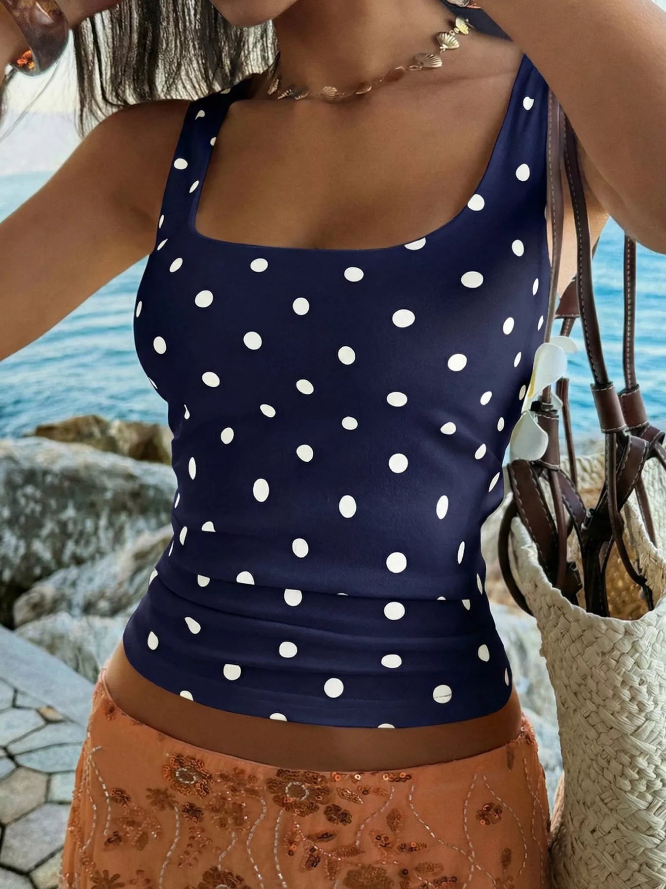 Woman wearing a navy blue tank top with white polka dots by the water.
