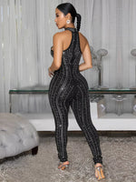 Woman in a black sequin jumpsuit standing in a room with a glass table and decorative items.