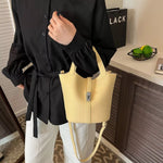 A person wearing a black long-sleeve button-up shirt and white pants carries a pale yellow pebbled faux-leather bucket bag with a front zipper and shoulder strap in an indoor setting.