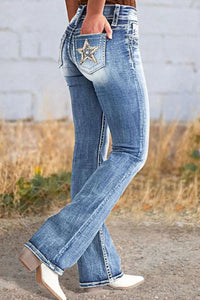 Flared jeans with a star pocket detail worn by a person, standing on a dirt path with grass and a wall in the background.