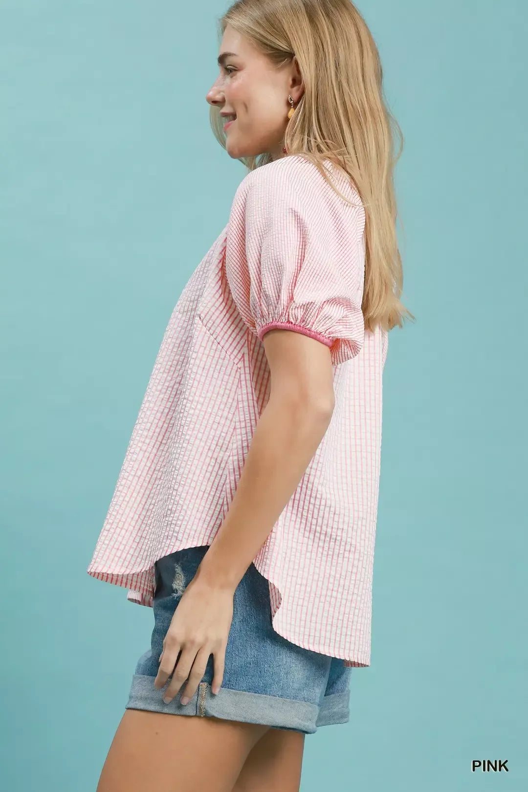 Woman wearing a pink checkered blouse and denim shorts against a light blue background