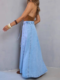 Person wearing a long denim skirt against a plain background