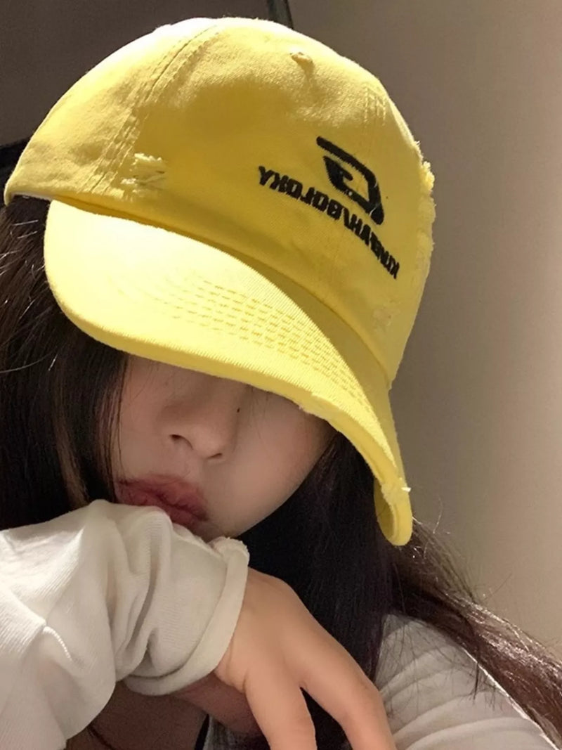 Person wearing a yellow cap with a logo, sitting against a neutral background