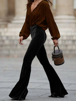 Person wearing a brown blouse and black flared pants, holding a small handbag.
