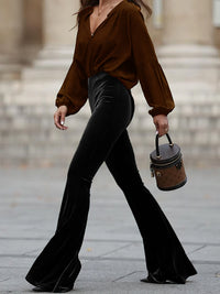 Person wearing a brown blouse and black flared pants, holding a small handbag.