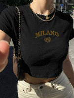 Person wearing a black t-shirt with 'MILANO' print, standing outdoors.