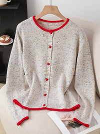 Knitted cardigan with red trim on a hanger against a neutral background