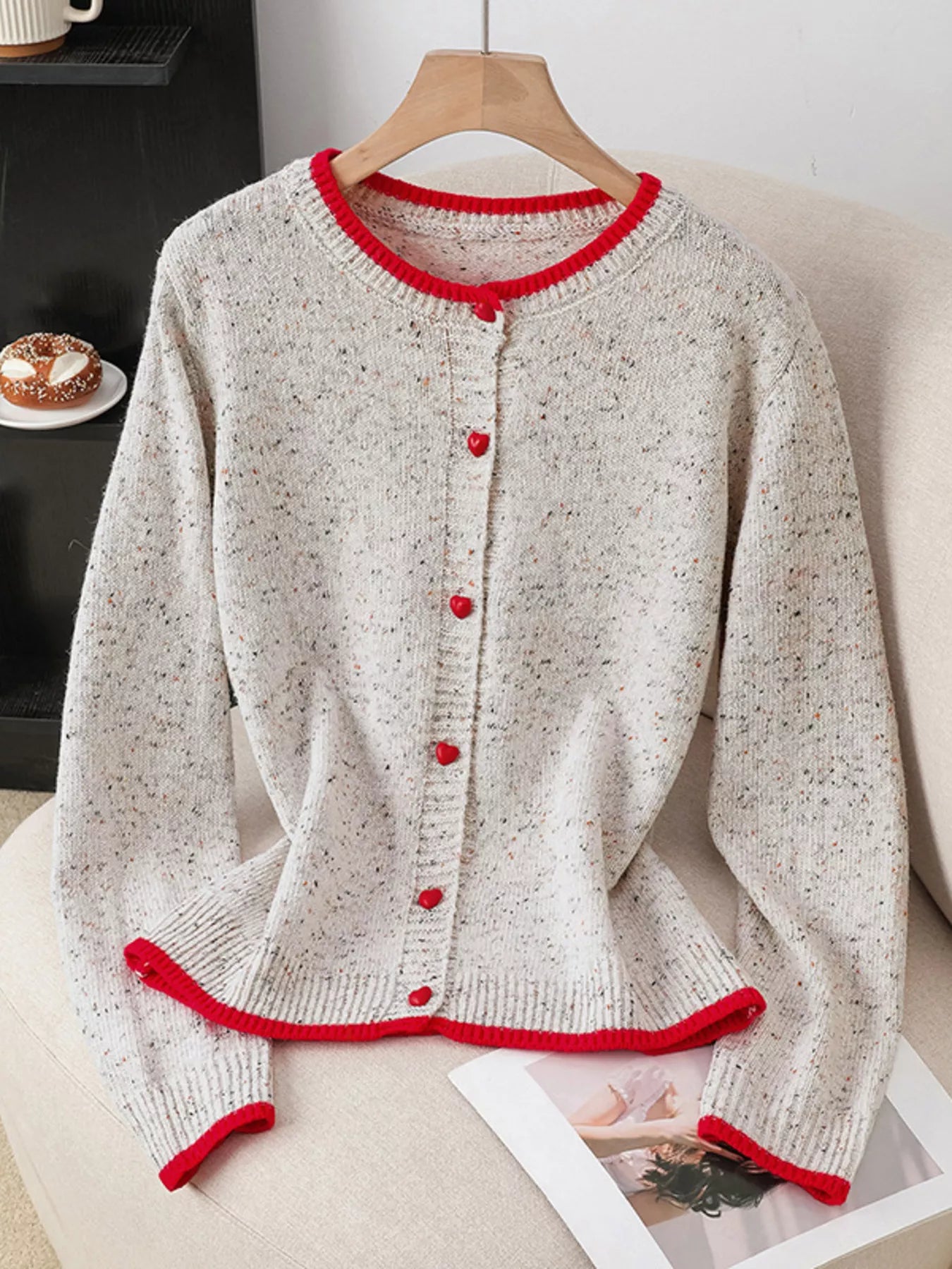 Knitted cardigan with red trim on a hanger against a neutral background