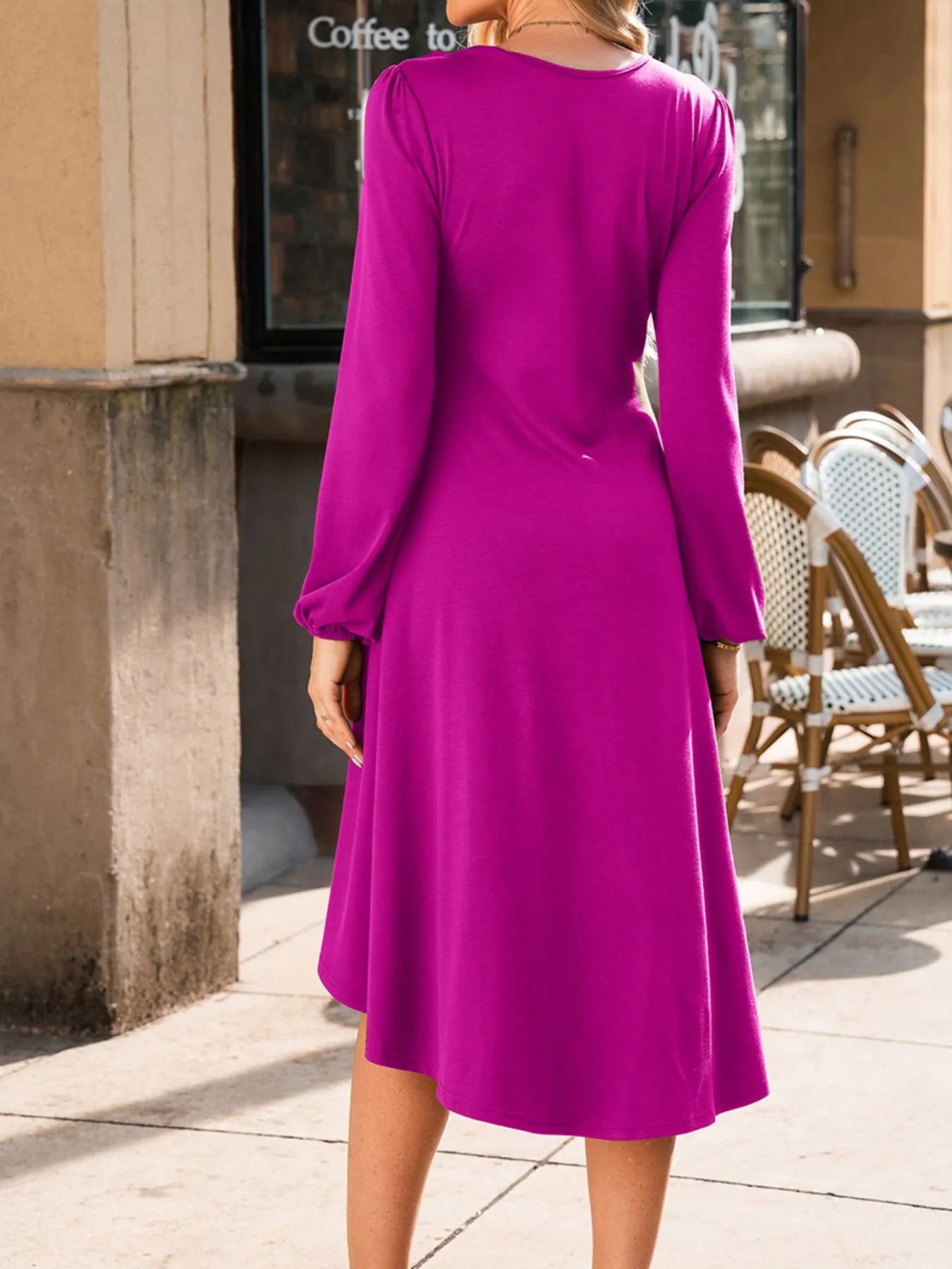 Person wearing a purple dress standing outdoors near a building entrance.