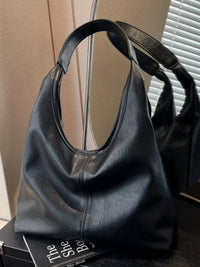Black leather handbag on a surface with a book underneath