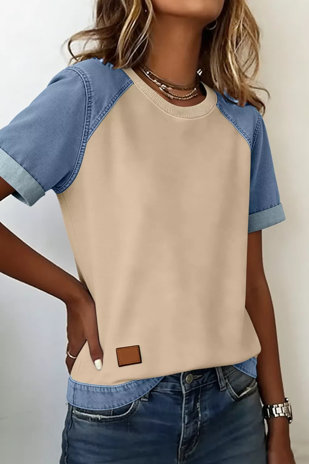 Person wearing a beige and blue color-blocked shirt with denim jeans on a plain background