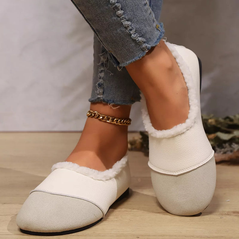 White slippers with fluffy lining worn by a person on a wooden floor.