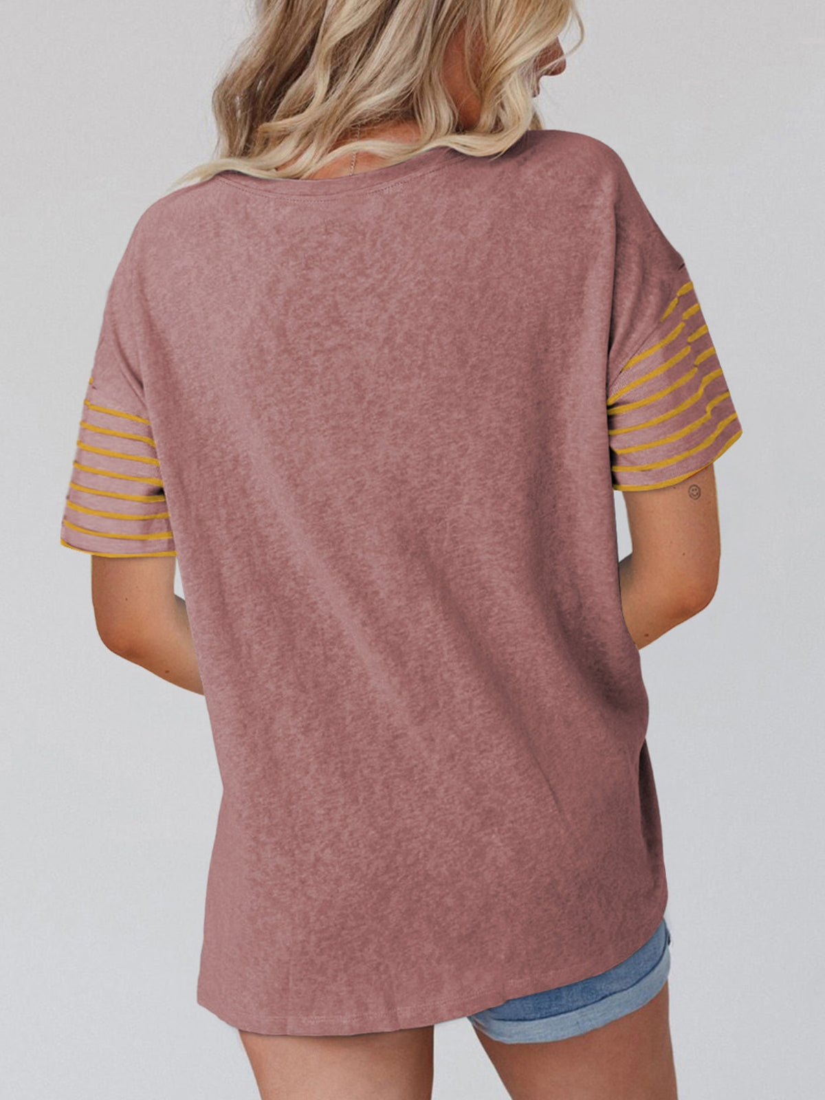 Person wearing a mauve t-shirt with yellow stripes on sleeves against a plain background