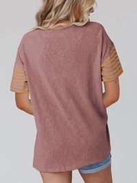 Person wearing a mauve t-shirt with yellow stripes on sleeves against a plain background