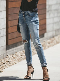 Person wearing ripped blue jeans and black high-heeled shoes on a sidewalk.