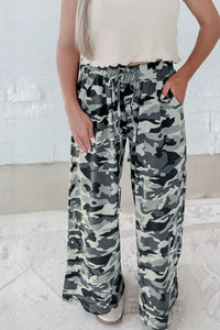 Camouflage pants worn by a person against a white brick wall.