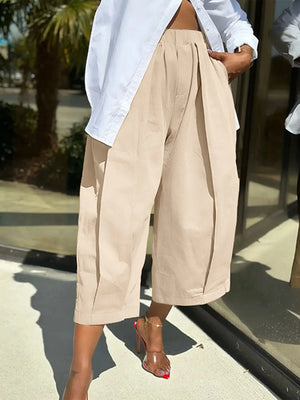 Person wearing beige wide-leg pants and a white shirt on a sidewalk.