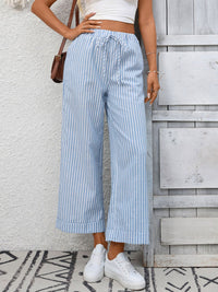 Person wearing blue and white striped pants with a white top against a wooden wall.