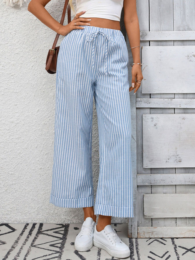 Person wearing blue and white striped pants with a white top against a wooden wall.