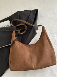 Brown leather handbag on a textured surface with a black jacket and white shirt underneath.