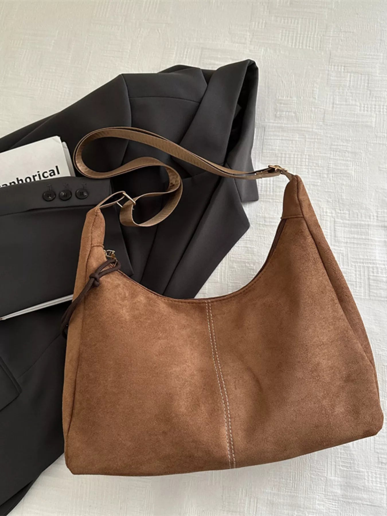 Brown leather handbag on a textured surface with a black jacket and white shirt underneath.
