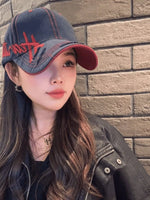 Woman wearing a denim cap with red accents against a brick wall.
