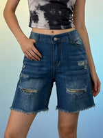 Person wearing tie-dye crop top and distressed denim shorts on a gradient background
