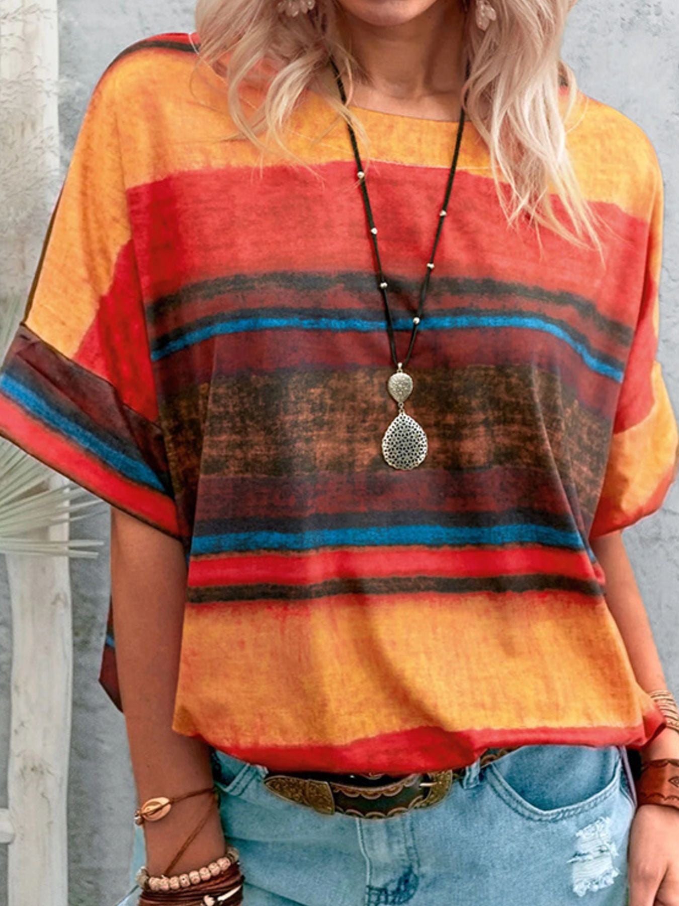 Person wearing a colorful striped shirt with a necklace and denim jeans.
