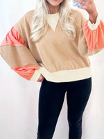 Person wearing a beige and pink long-sleeve top with black pants on a white background