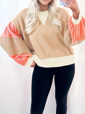 Person wearing a beige and pink long-sleeve top with black pants on a white background