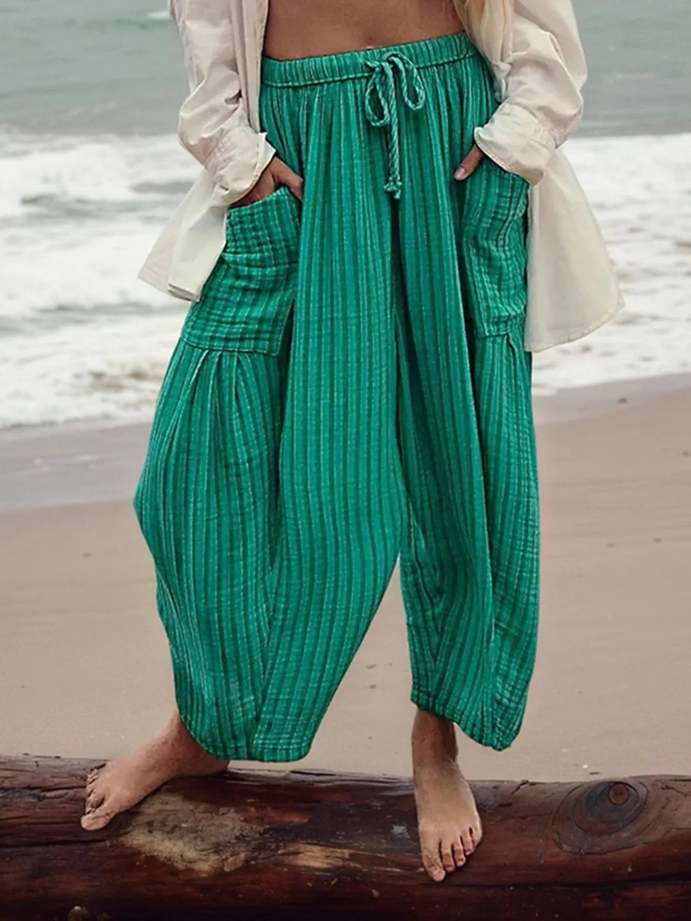 Person wearing green pants standing on a beach with ocean in the background
