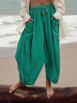 Person wearing green pants standing on a beach with ocean in the background
