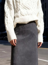 Person wearing a white cable knit sweater and gray skirt on an urban street.