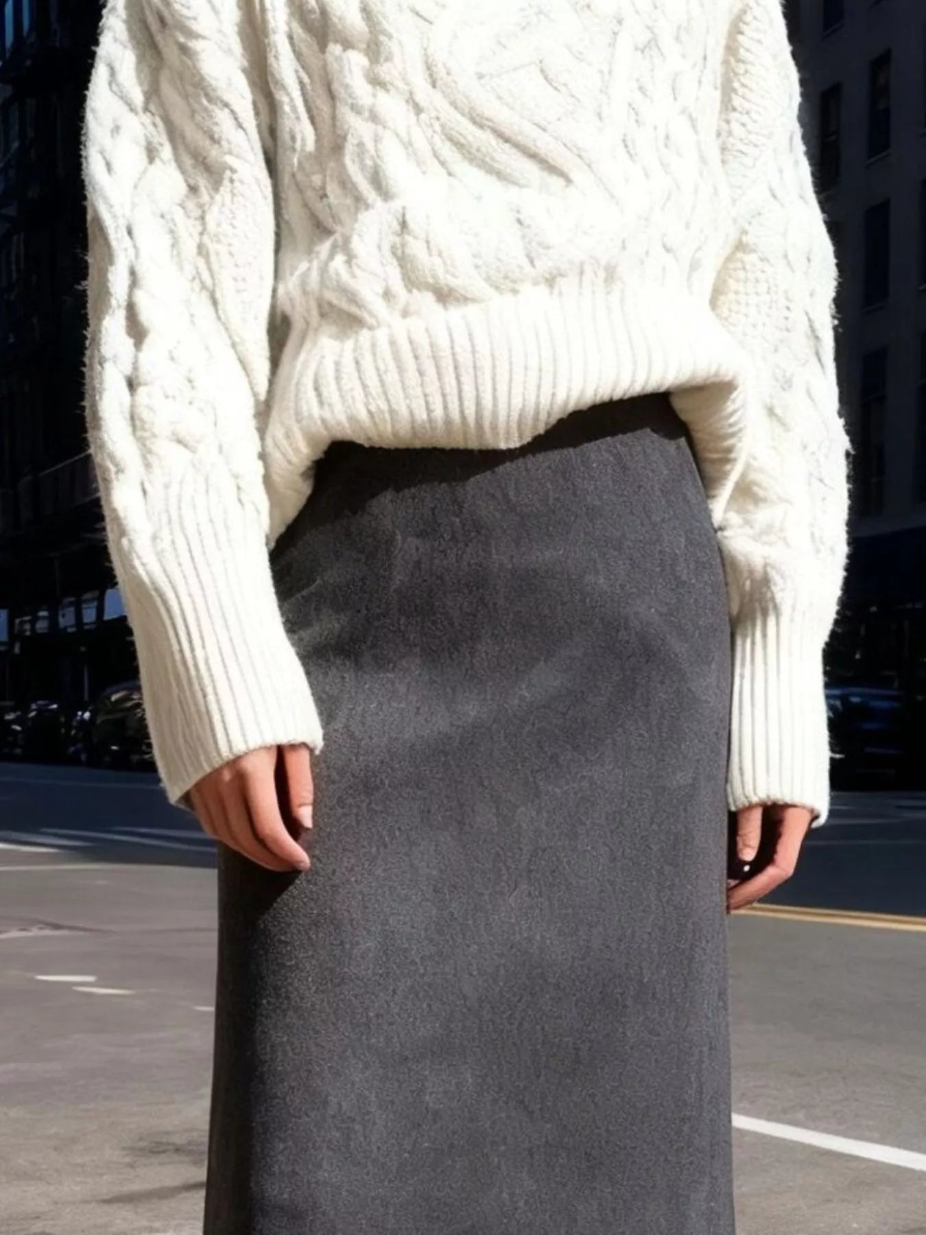Person wearing a white cable knit sweater and gray skirt on an urban street.