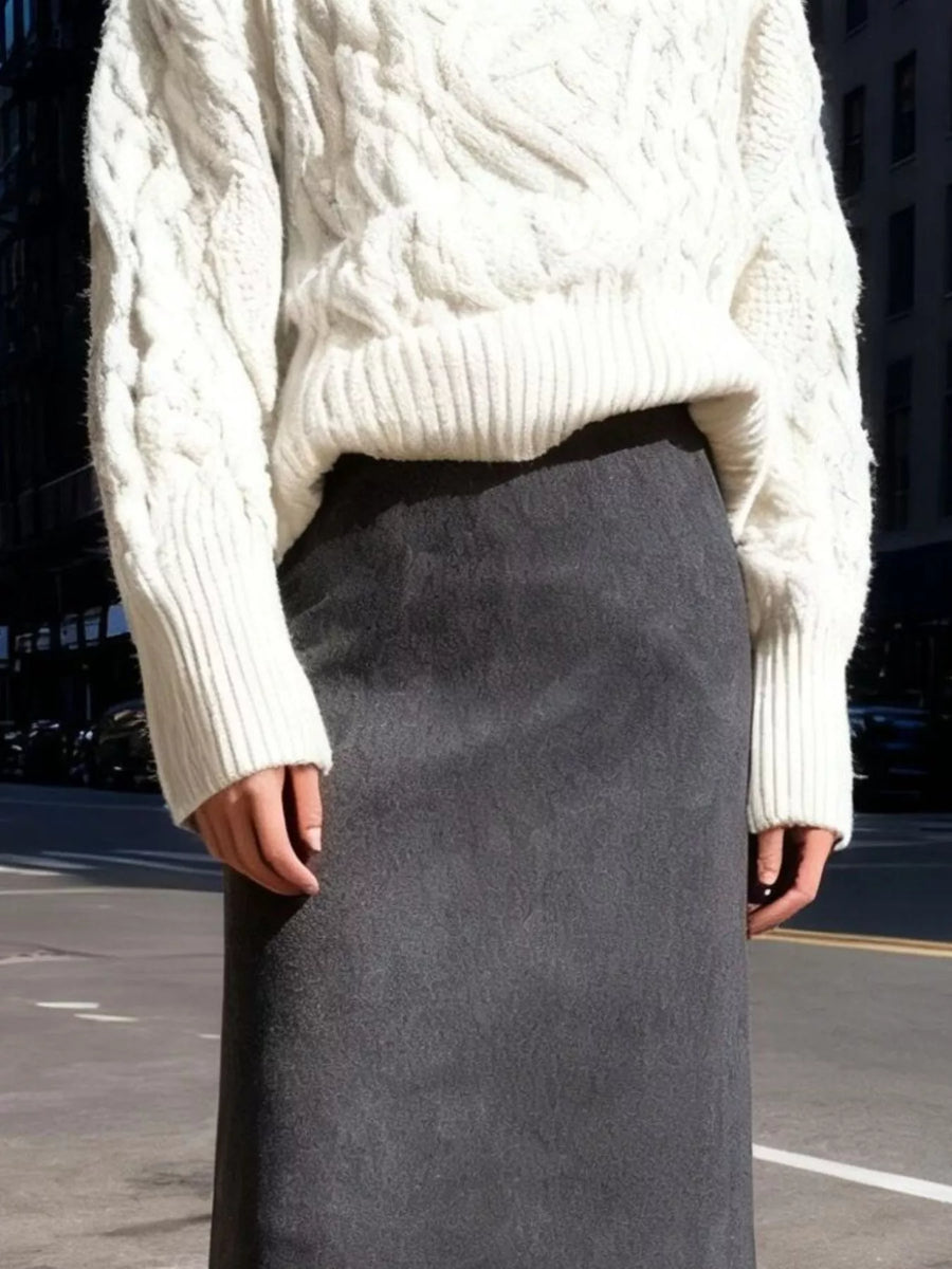 Person wearing a white cable knit sweater and gray skirt on an urban street.