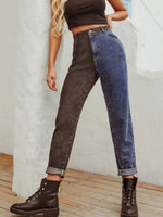Person wearing high-waisted dark brown and blue jeans with brown boots against a light gray wall.