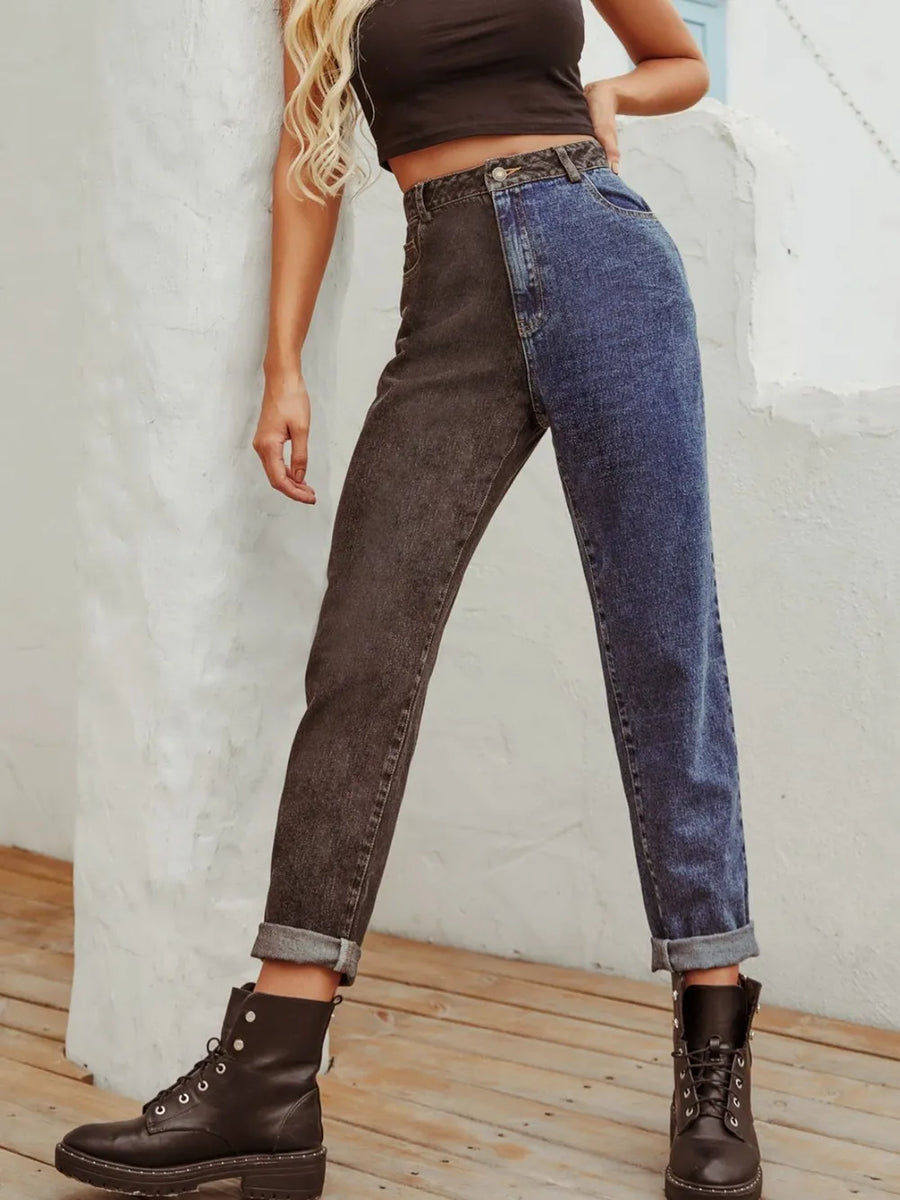 Person wearing high-waisted dark brown and blue jeans with brown boots against a light gray wall.