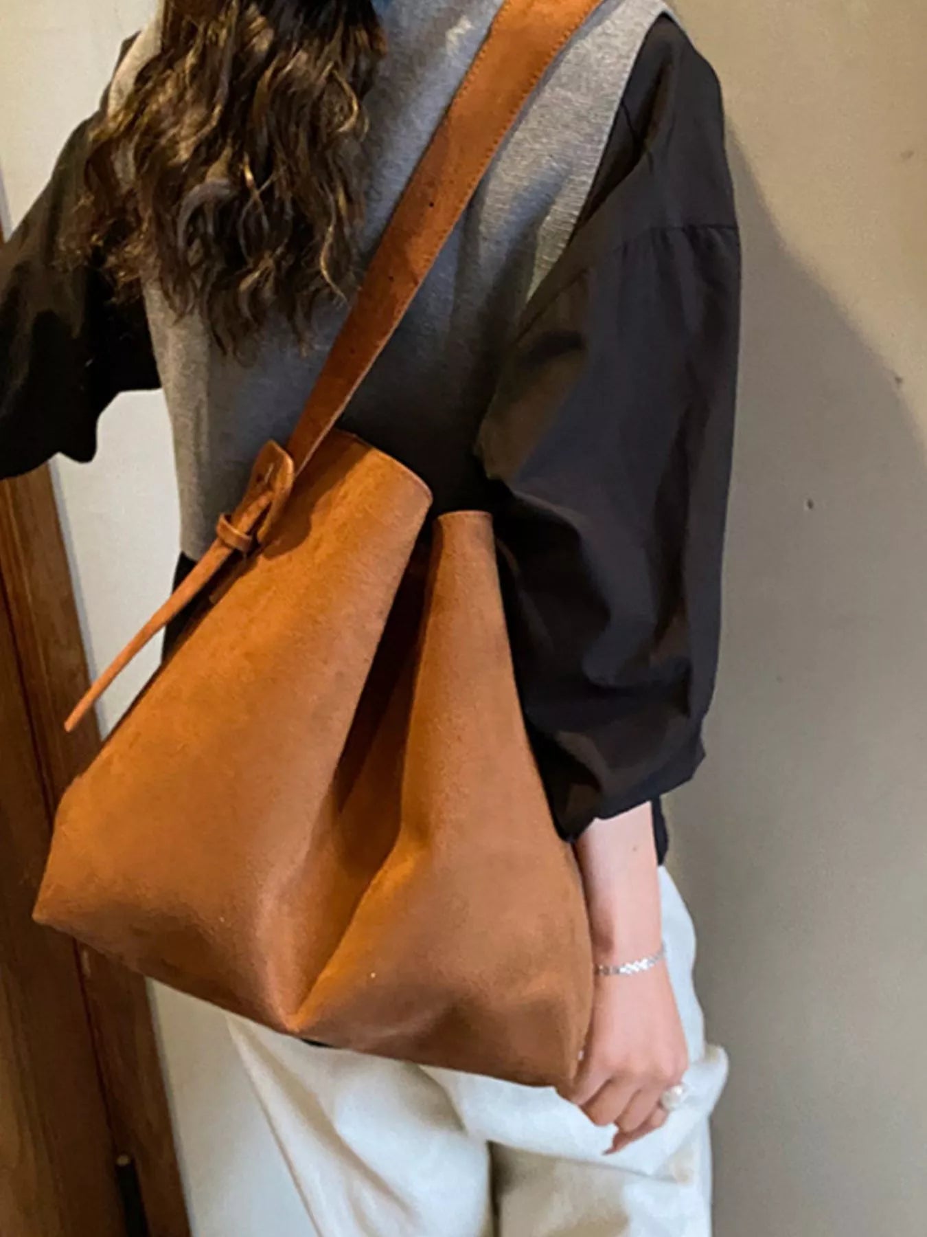 Person wearing a brown leather shoulder bag against a neutral background