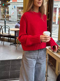 Woman in a red sweater holding a coffee cup in an urban setting