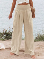 Person wearing beige wide-leg pants on a beach with a light blue wall in the background