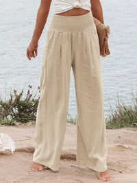 Person wearing beige wide-leg pants on a beach with a light blue wall in the background