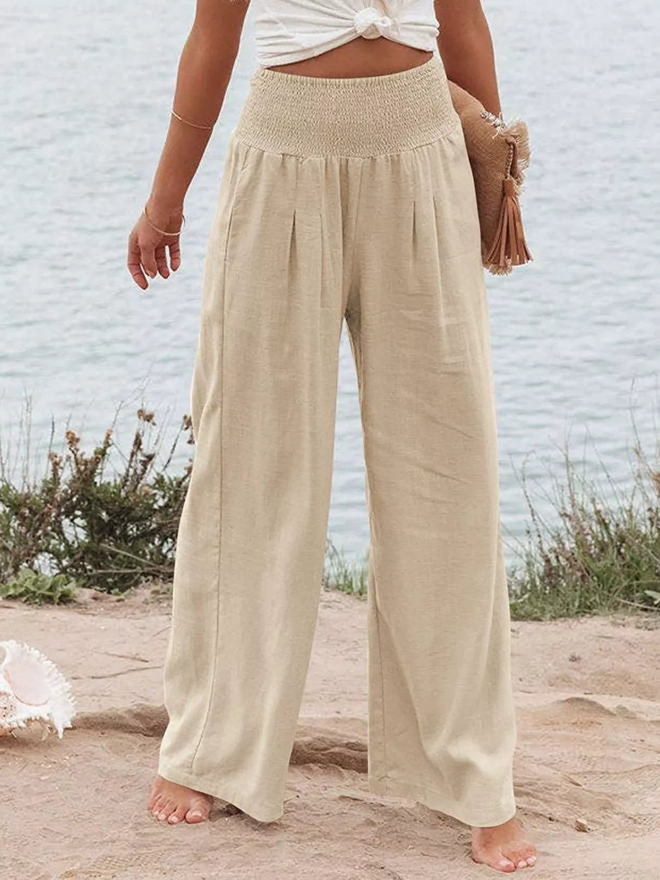 Person wearing beige wide-leg pants on a beach with a light blue wall in the background